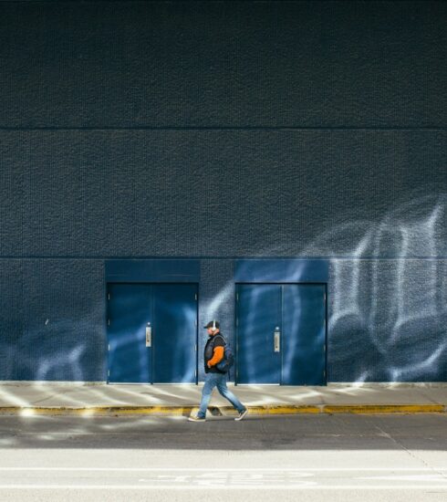 Person walks past doors in the sunlight.